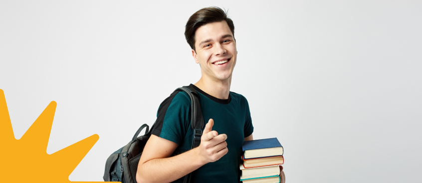 Estudiante con libros sonríe mientras se dirige a la sala de multimedia para realizar proyectos de diseño industrial en Bogotá.